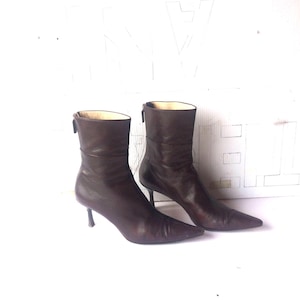 May include: A pair of brown leather ankle boots with pointed toes and stiletto heels. The boots have a zipper on the back and a smooth, polished finish. The heels are approximately 3 inches high.