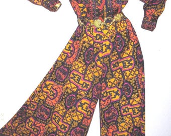 Könnte beinhalten: Ein Vintage-Jumpsuit mit einem auffälligen geometrischen Muster in Orange, Gelb, Schwarz und Lila. Das langärmlige Oberteil hat einen Kragen, und die weite Hose ist mit einem goldfarbenen Gürtel in der Taille gerafft. Der Jumpsuit wird auf einer Schaufensterpuppe präsentiert.