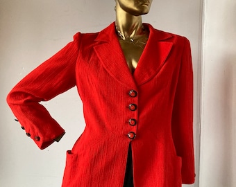 May include: A vibrant red blazer with a textured fabric, featuring a notched collar, four dark buttons, and two front pockets. The blazer is displayed on a gold mannequin, showcasing its tailored fit and design.