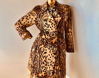 Puede incluir: Un maniquí dorado exhibe un abrigo de doble botonadura con estampado de leopardo y un cinturón decorativo. El abrigo presenta un patrón de manchas marrones y negras. El maniquí está frente a una pared blanca.