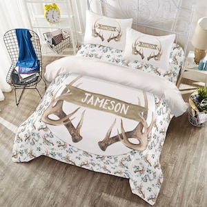 May include: White bedding set with a brown and white deer antler design. The duvet cover features a large antler design with a banner that reads "Jameson". The pillowcases have a smaller antler design with the word "Jameson" on each pillowcase.