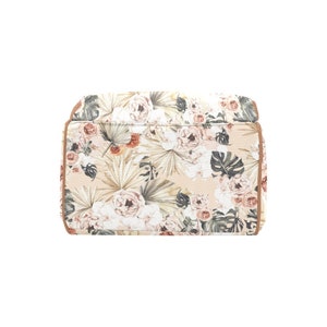 May include: A beige canvas tote bag with a floral print featuring pink and white flowers, green leaves, and brown accents. The bag has a brown leather trim.