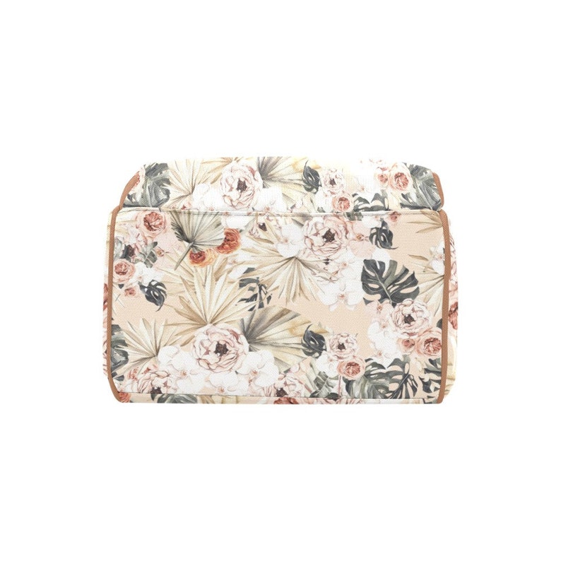 May include: A beige canvas tote bag with a floral print featuring pink and white flowers, green leaves, and brown accents. The bag has a brown leather trim.