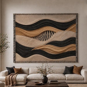 May include: A rectangular woven wall hanging featuring a layered, abstract landscape design with undulating horizontal bands in black, tan, and beige. A central section displays a black and beige zebra stripe pattern, and the edges are fringed.