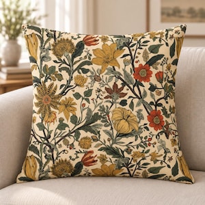 May include: A square throw pillow featuring a cream-colored background with a dense botanical pattern of yellow, orange, and red flowers, dark green leaves, and brown stems. The design covers the entire front surface of the pillow.