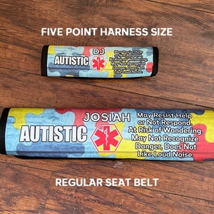 May include: Two colorful seat belt covers with the word "AUTISTIC" printed on them. The covers also include a red star of life symbol and text that reads "May Resist Help or Not Respond. At Risk of Wandering. May Not Recognize Danger, Does Not Like Loud Noise." One cover is labeled "DJ" and the other is labeled "JOSIAH". The top cover is labeled "FIVE POINT HARNESS SIZE" and the bottom cover is labeled "REGULAR SEAT BELT".