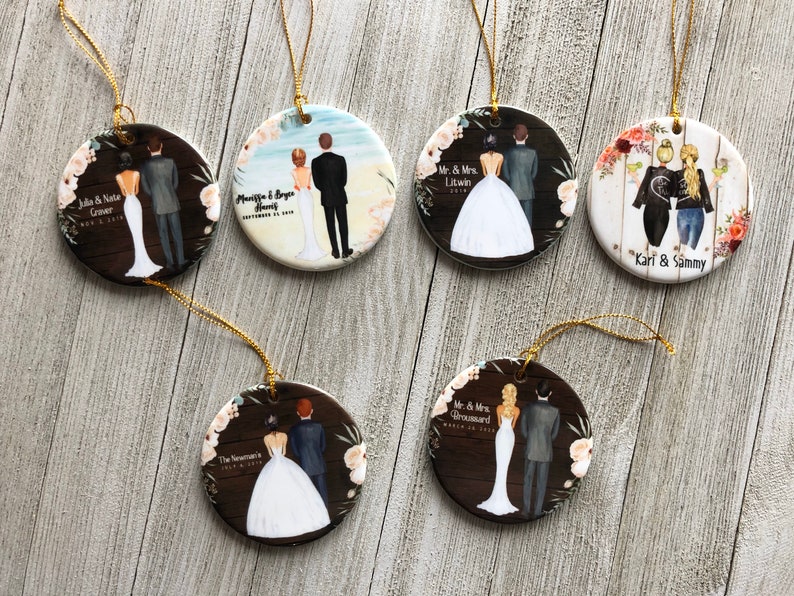 May include: Six round ceramic ornaments with gold string hangers. Each ornament features a different couple with a personalized name and date. The ornaments are decorated with floral designs and a woodgrain background.