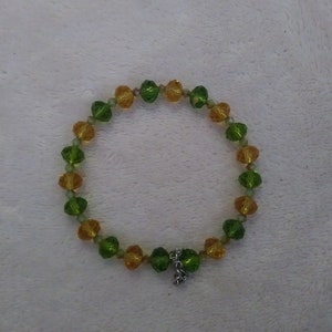 May include: A green and gold beaded bracelet with a silver charm.