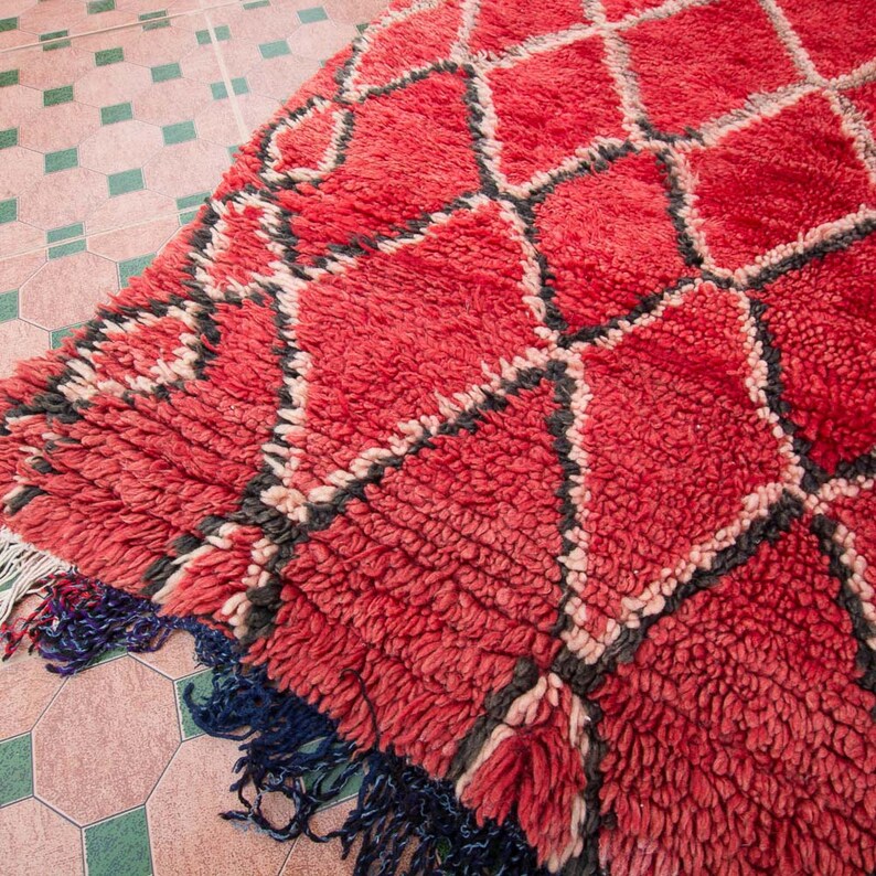 May include: A red and black Moroccan rug with a diamond pattern. The rug has a thick, fluffy pile and is made of wool.