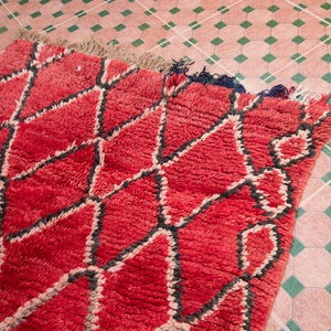 May include: A red and black Moroccan rug with a geometric pattern. The rug is made of wool and has a soft, plush texture.