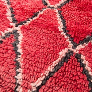 May include: Close-up of a red and pink woven rug with a geometric pattern. The rug has a soft, fuzzy texture.