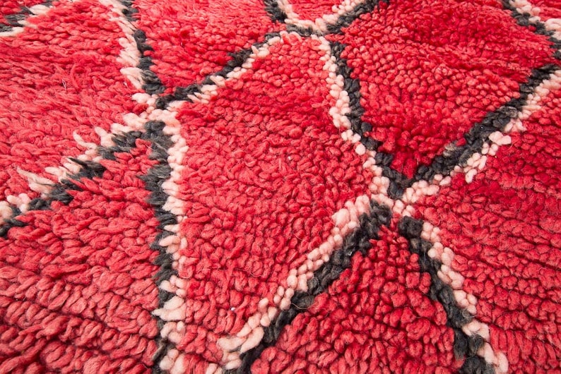 May include: Close-up of a red and pink woven rug with a geometric pattern. The rug has a soft, fuzzy texture.