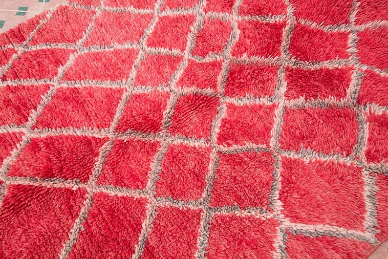 May include: A red and gray patterned rug with a fluffy texture. The rug has a geometric design with squares and diamonds.