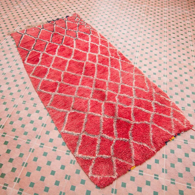 May include: A red and white Moroccan rug with a diamond pattern. The rug is made of wool and has a soft, fluffy texture.