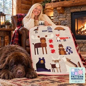 May include: A quilt featuring a light-colored background with geometric animal illustrations including a moose, fox, beaver, bear, deer, and wolf, accented by red maple leaves. The quilt has a thin pink border and a repeating pattern of woodland creatures.