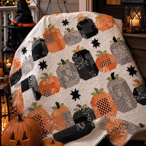 May include: A quilt featuring a repeating pattern of pumpkins in orange, black, and grey on a white background with black star accents. The fabric displays various geometric and floral prints within the pumpkin shapes, finished with a black and white striped edge.