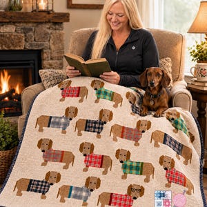 May include: A beige quilt featuring a repeating pattern of brown dachshunds wearing various colourful plaid sweaters. The quilt has a dark blue border and includes a logo in the bottom right corner that reads Pattern Warehouse Quilting Crochet Longarm.