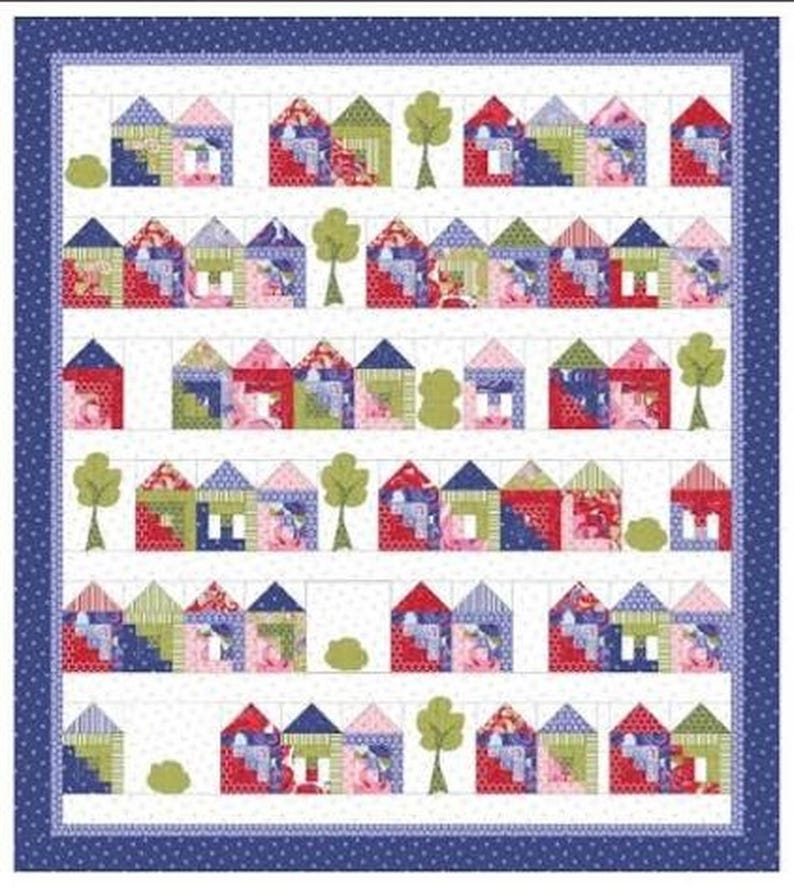 Op de afbeelding: Een quilt met een herhalend patroon van kleurrijke stoffen huisjes en groene bomen, gerangschikt in rijen op een witte achtergrond met een gestippelde textuur. Het geheel is omlijst door een donkerblauwe rand met witte stippen.