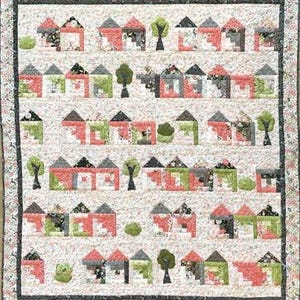 Op de afbeelding: Een rechthoekige quilt met een herhalend patroon van kleine huisjes en bomen in tinten rood, groen, zwart en wit. Het ontwerp is gerangschikt in horizontale rijen tegen een lichte bloemenachtergrond, afgewerkt met een donkere bloemenrand.