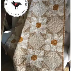May include: A quilt titled Cotton Daisies featuring a repeating floral pattern with white petals and golden-brown centres. The text reads Cotton Daisies, Wall Hanging: 114 cm x 114 cm, Lap Quilt: 114 cm x 160 cm, and a logo with a bird and Laugh Yourself Into Stitches.