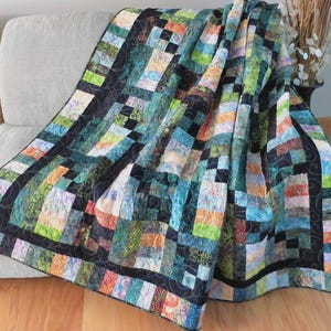 May include: A colorful patchwork quilt with a geometric design. The quilt features a variety of fabrics in shades of blue, green, orange, and black. The quilt is draped over a sofa, showcasing its texture and pattern.