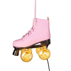 May include: A pink roller skate with four light bulbs for wheels. The skate is hanging from a black cord.