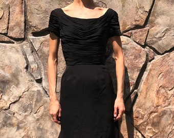 May include: A black sleeveless dress with a fitted bodice and a slightly flared skirt. The dress has a scoop neckline and a gathered detail at the waist.