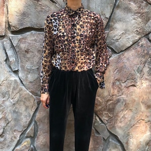 Puede incluir: Un pantalón negro plisado de cintura alta con una blusa de estampado de leopardo marrón y dorado.