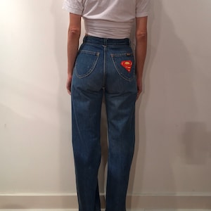 May include: A pair of blue denim jeans with a Superman logo patch on the back pocket.