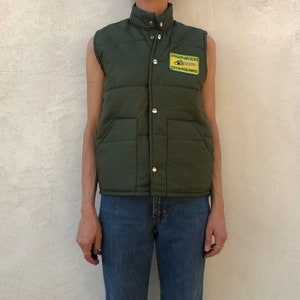 May include: A dark green quilted vest with a snap closure and a patch on the front that reads "Pioneer Chainsaws".