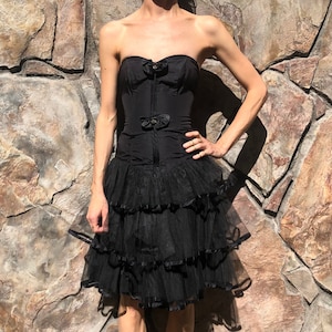 May include: A black strapless dress with a fitted bodice and a layered tulle skirt. The bodice has a satin finish and features a bow detail at the bust.