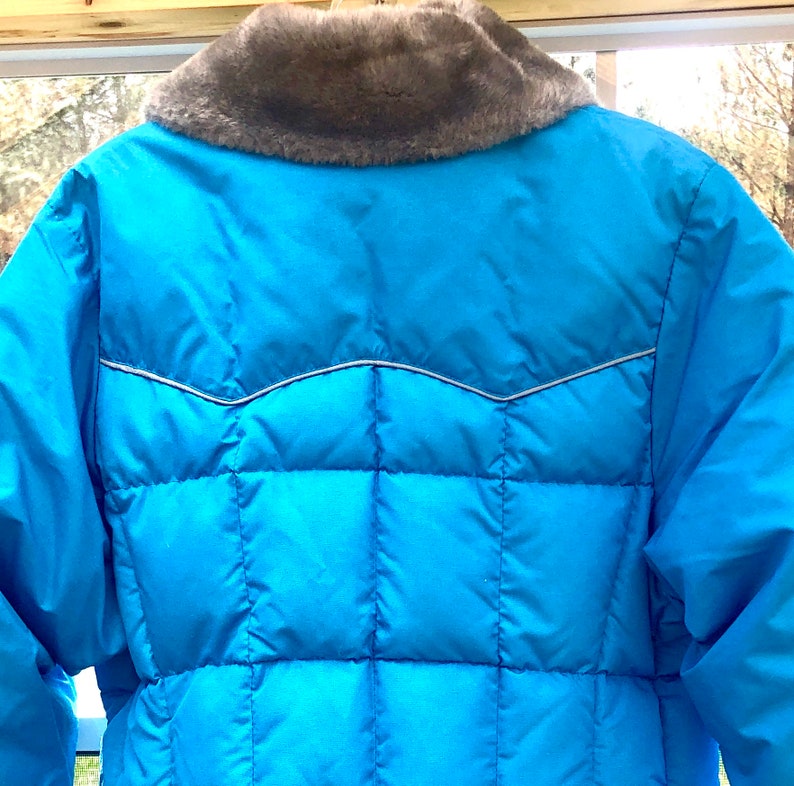 May include: A blue puffer jacket with a faux fur collar. The jacket has a quilted design and a silver zipper.