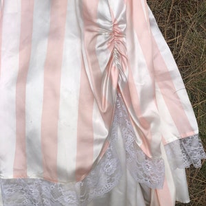May include: A pink and white striped satin skirt with a white lace trim. The skirt has a gathered detail at the back.