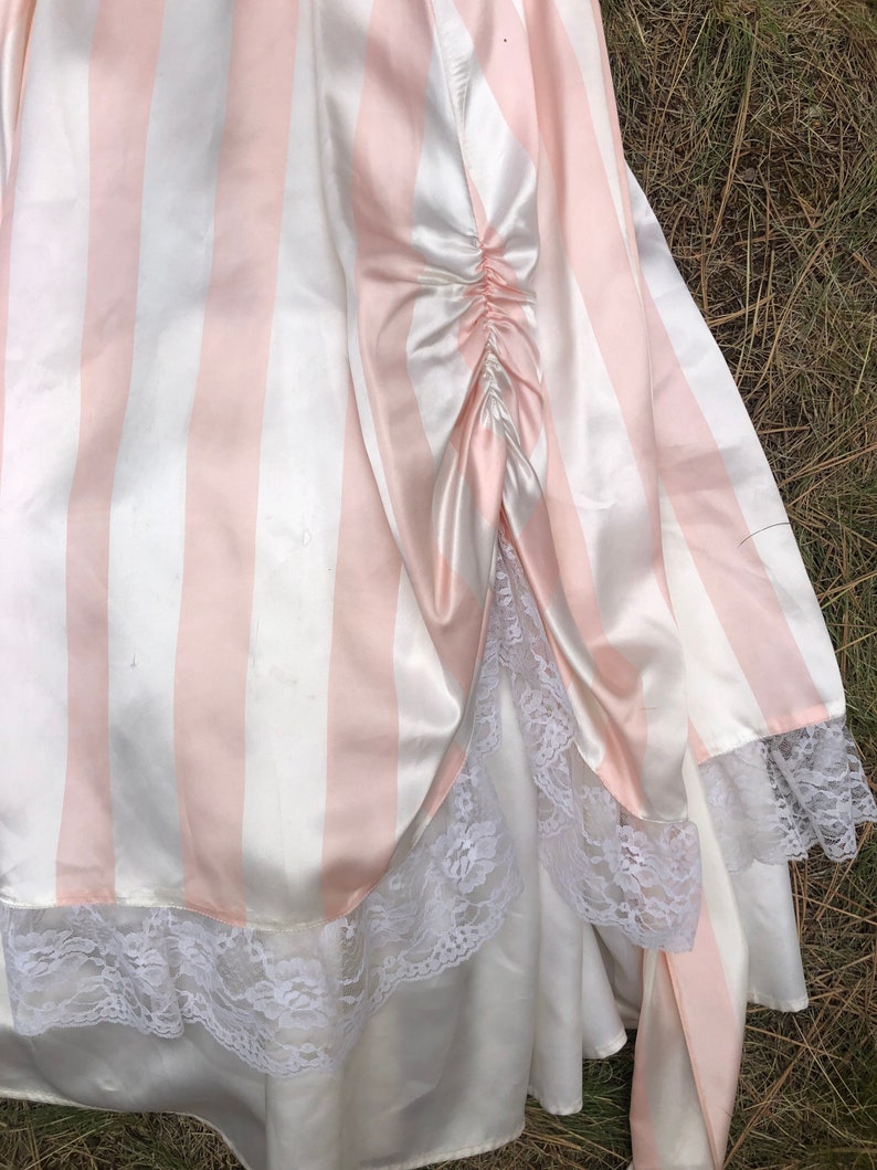 May include: A pink and white striped satin skirt with a white lace trim. The skirt has a gathered detail at the back.