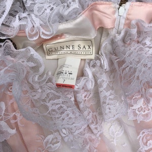 May include: A white lace dress with a pink satin lining. The dress has a label that reads "Gunne Sax by Jessica McClintock" and a size tag that says "Size 7".