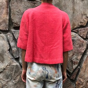 May include: A coral pink short-sleeved jacket with a high neckline and a textured fabric.