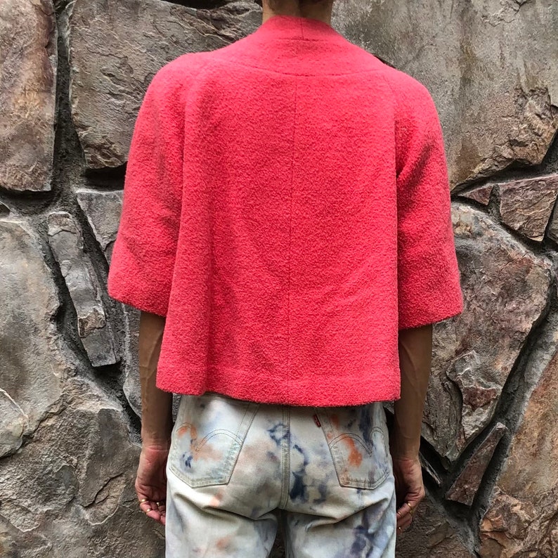 May include: A coral pink short-sleeved jacket with a high neckline and a textured fabric.