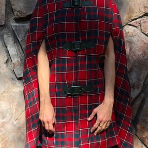 May include: Red and black plaid cape with black leather buckles. The cape has a high collar and is open in the front.