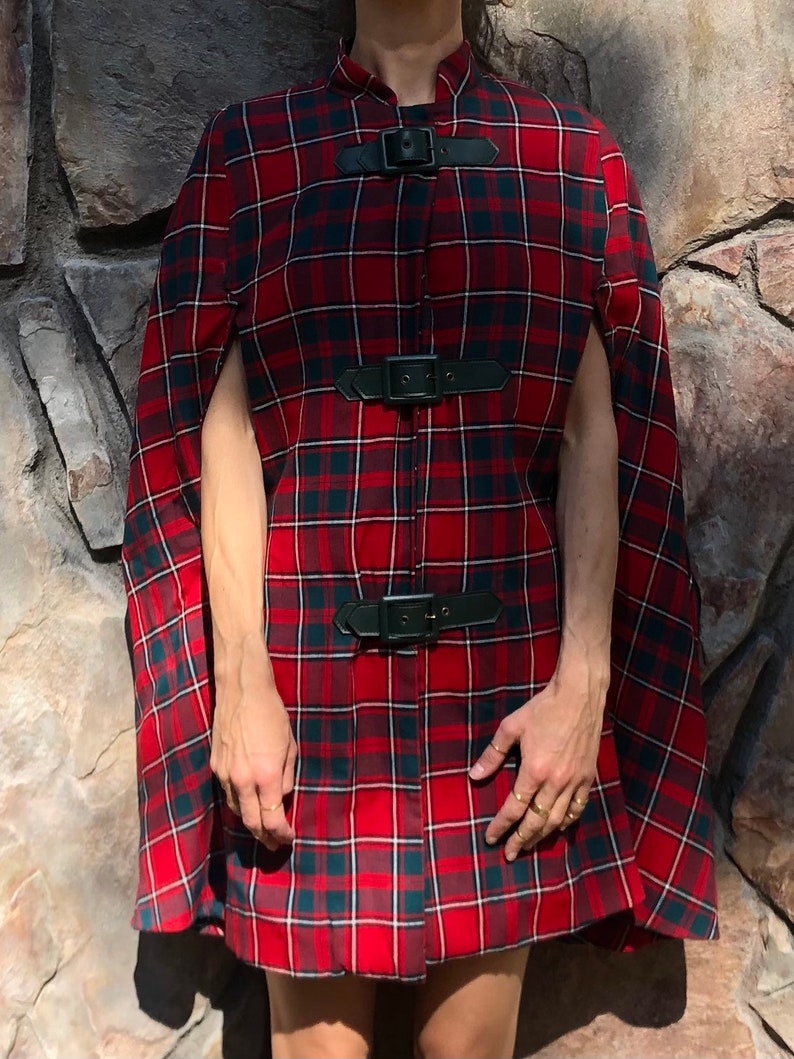 May include: Red and black plaid cape with black leather buckles. The cape has a high collar and is open in the front.