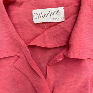 May include: A coral pink button-up shirt with a white label that reads "Marjone Seattle".