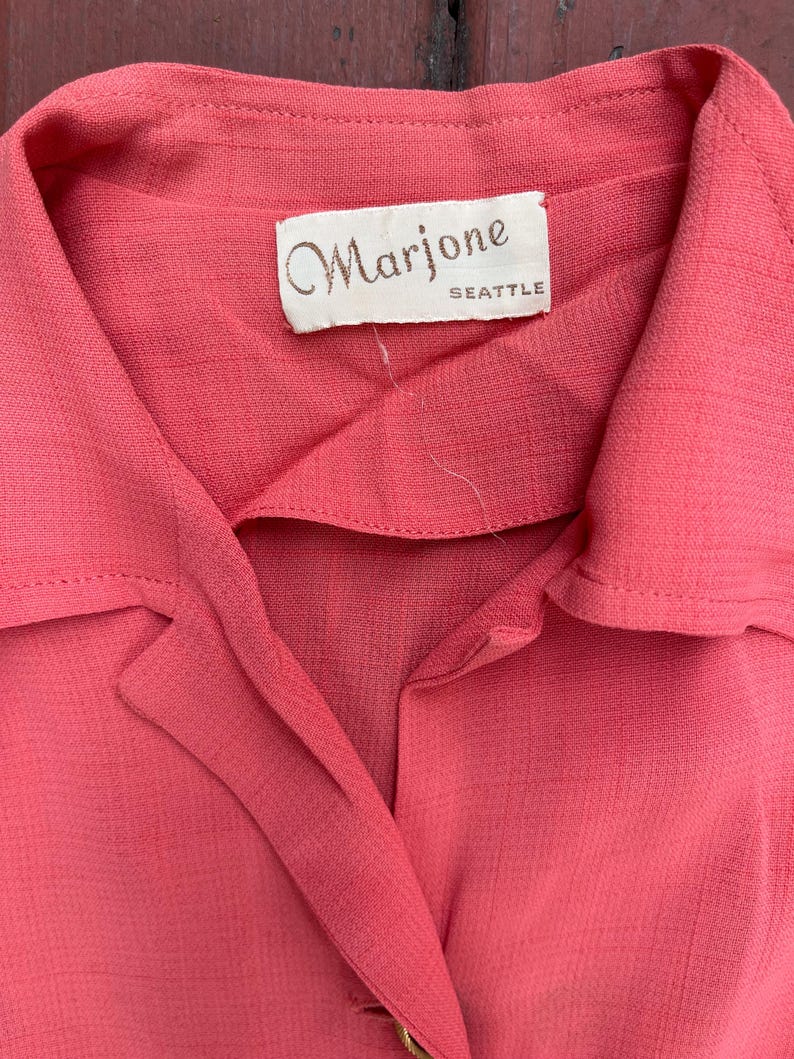 May include: A coral pink button-up shirt with a white label that reads "Marjone Seattle".