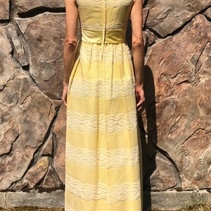 May include: A yellow maxi dress with white lace detailing and a satin sash. The dress has a sleeveless design and a back zipper closure.
