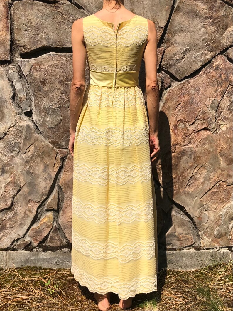 May include: A yellow maxi dress with white lace detailing and a satin sash. The dress has a sleeveless design and a back zipper closure.