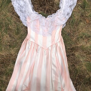 May include: A pink and white striped dress with a white lace overlay and off-the-shoulder neckline.