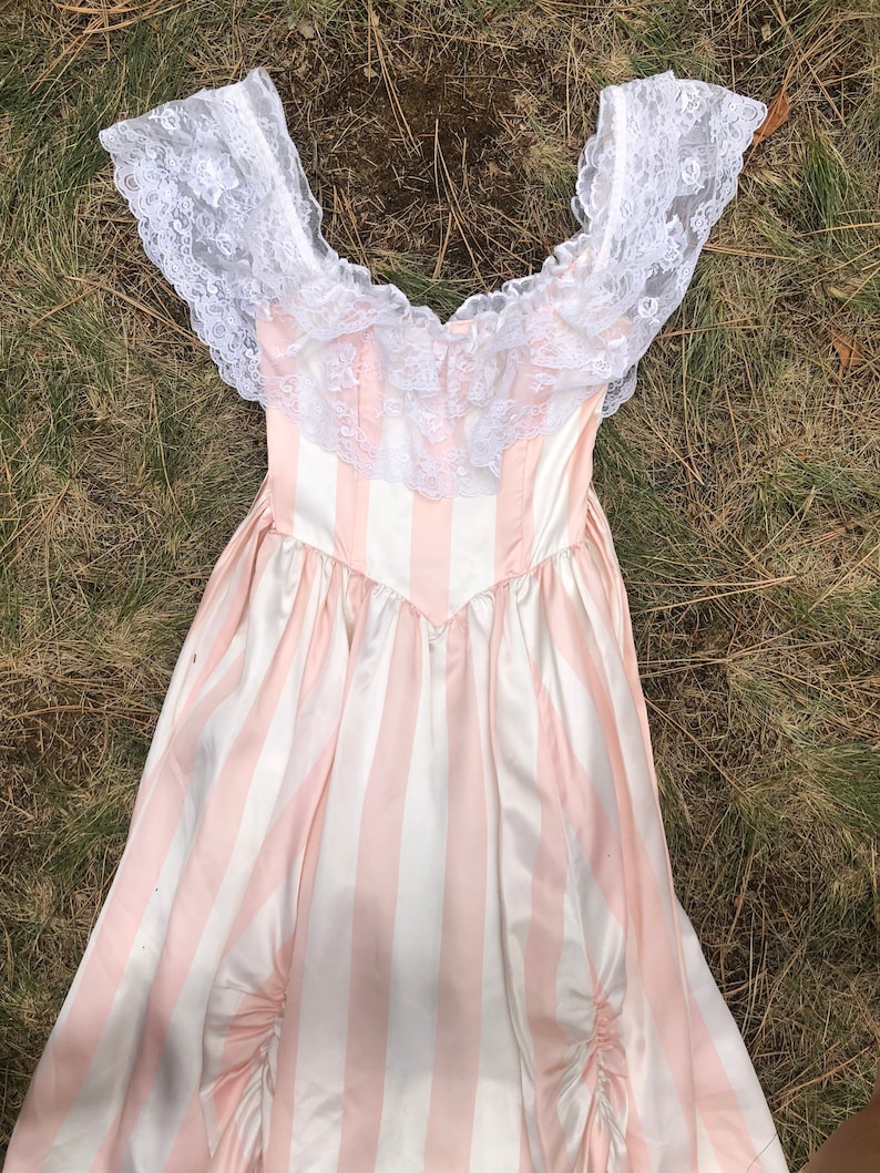 May include: A pink and white striped dress with a white lace overlay and off-the-shoulder neckline.