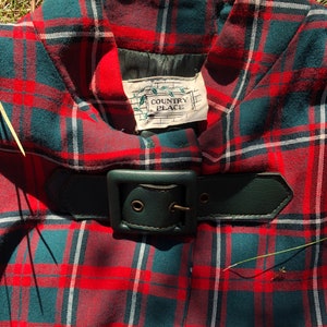 May include: Red, green, and white plaid skirt with a black leather belt and buckle. The skirt has a label that reads "Country Place".