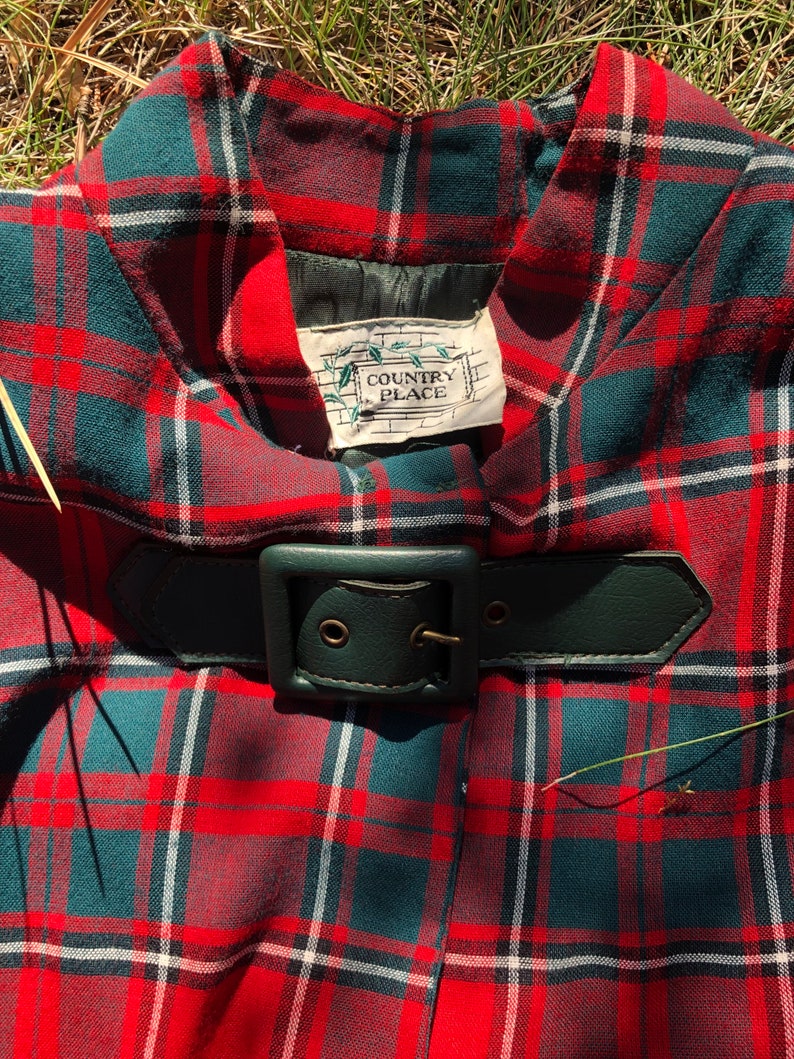 May include: Red, green, and white plaid skirt with a black leather belt and buckle. The skirt has a label that reads "Country Place".
