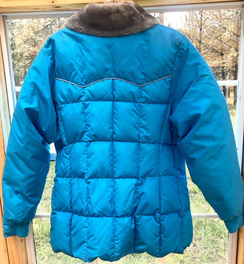 May include: A blue puffer jacket with a faux fur collar. The jacket has a quilted design and a slightly fitted silhouette.