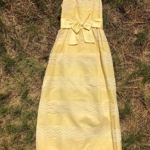 May include: A yellow sleeveless maxi dress with a white lace overlay and a satin bow at the waist.