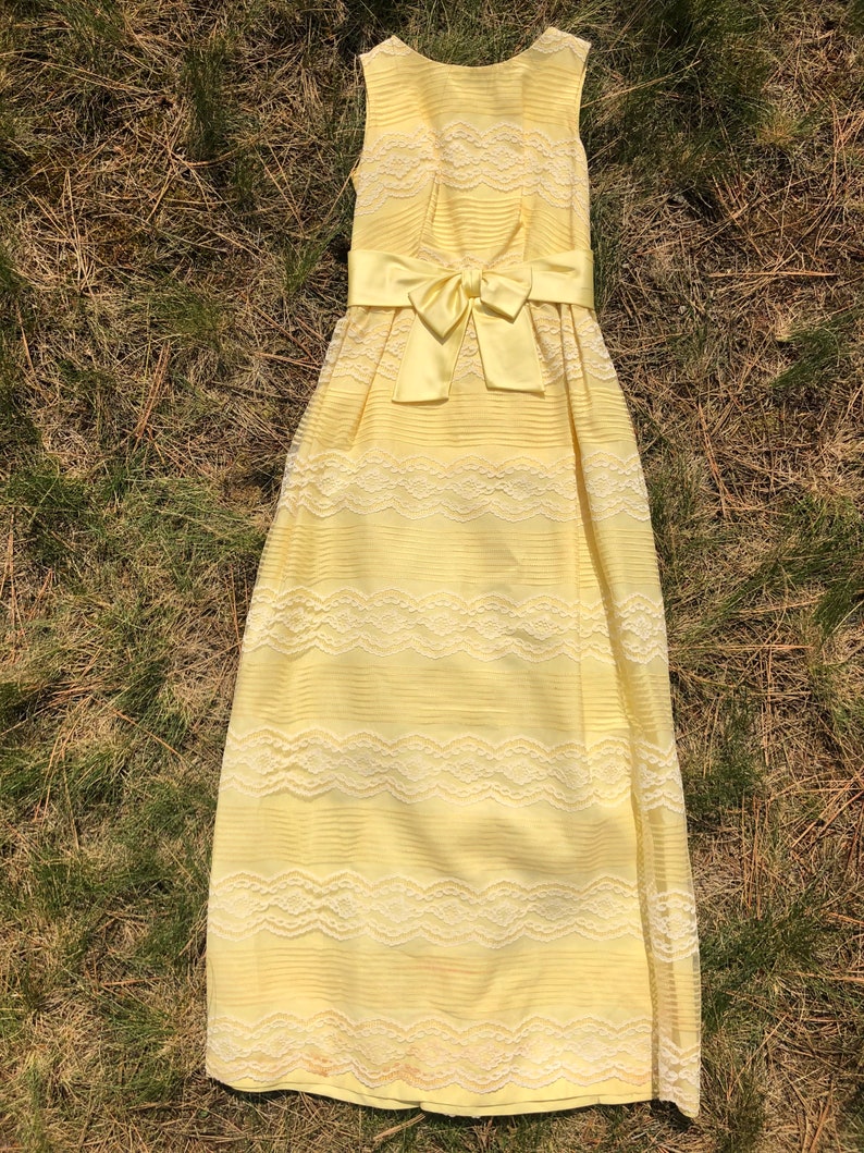 May include: A yellow sleeveless maxi dress with a white lace overlay and a satin bow at the waist.